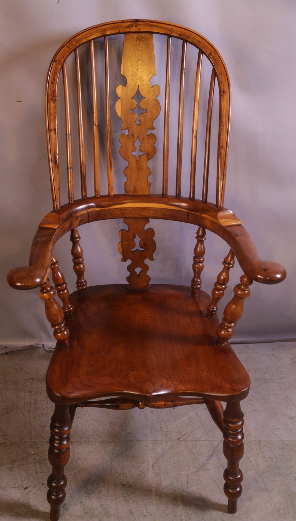 An antique yew wood high-back Windsor armchair featuring a pierced decorative splat, shaped pad arms, turned spindles, and a contoured wooden seat.
