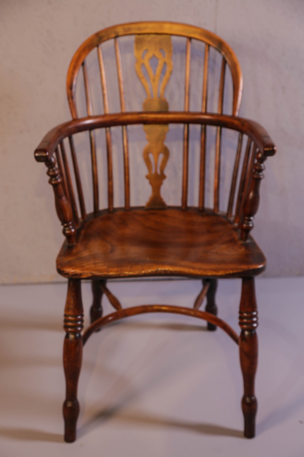 An antique yew wood low back Windsor chair featuring a contoured saddle seat, pierced splat back, turned spindles, and a curved stretcher connecting turned legs.
