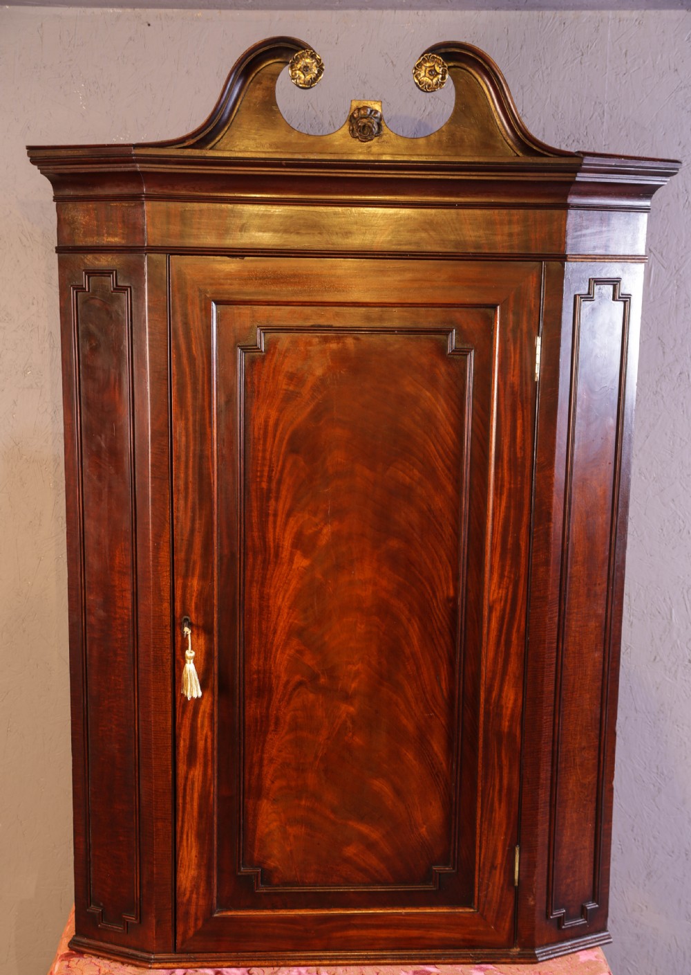 Georgian mahogany corner cupboard with a swan-neck pediment, carved gilt rosettes, and a fielded flame mahogany single door.