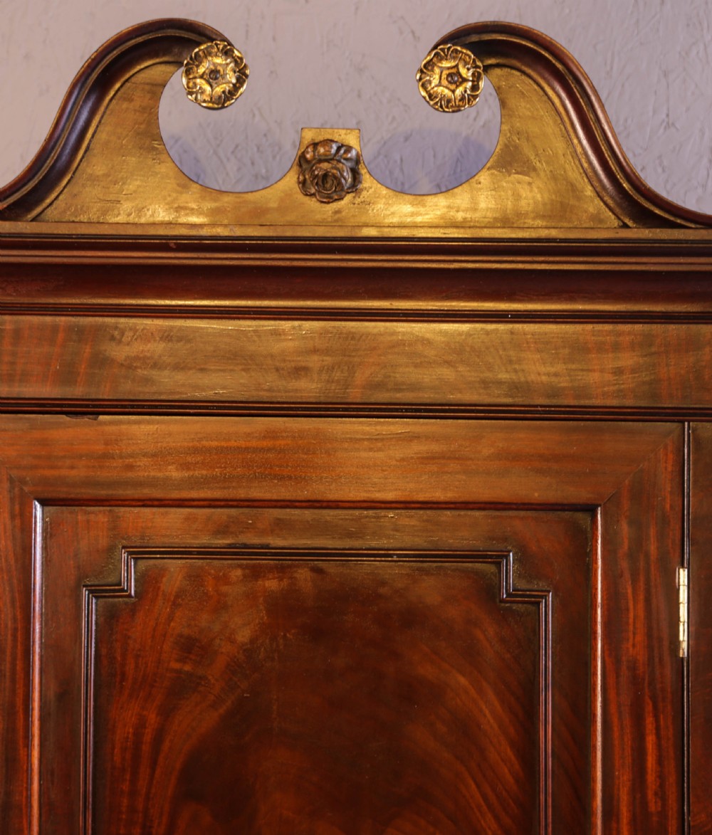 Georgian mahogany corner cupboard with a swan-neck pediment, carved gilt rosettes, and a fielded flame mahogany single door. View IV