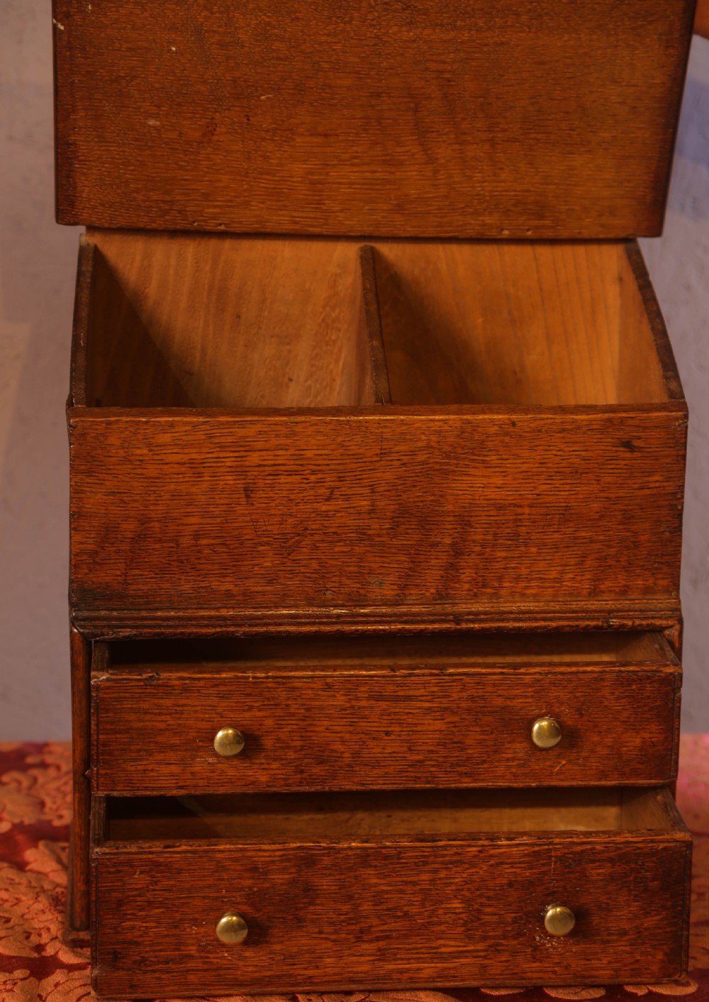 An antique warm brown oak candle box featuring a sloped lid, brass stud details on the shaped crest, and two drawers with brass knobs. View III