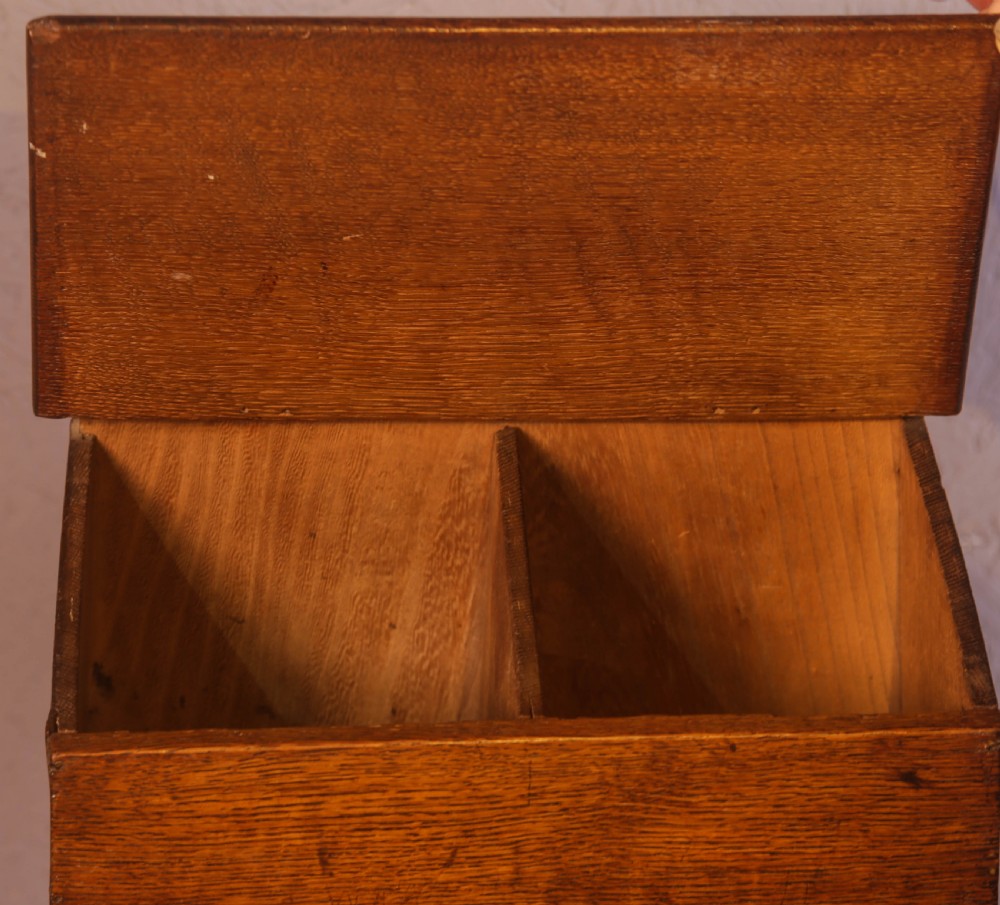 An antique warm brown oak candle box featuring a sloped lid, brass stud details on the shaped crest, and two drawers with brass knobs. View V