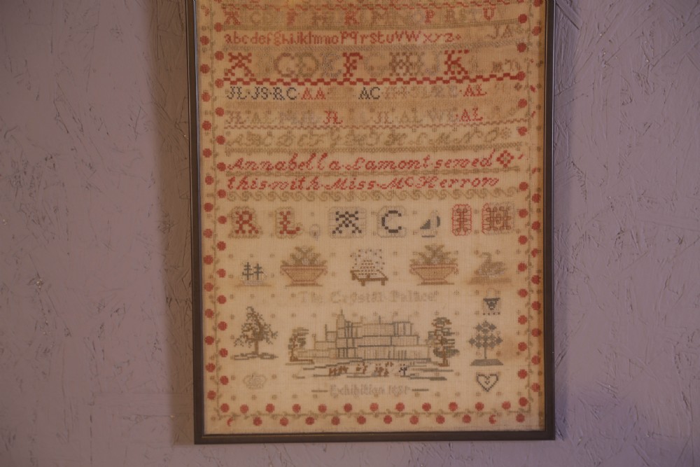 Framed 1851 Victorian needlework sampler featuring alphabets, numbers, and an embroidered depiction of the Crystal Palace on a linen ground. View VI