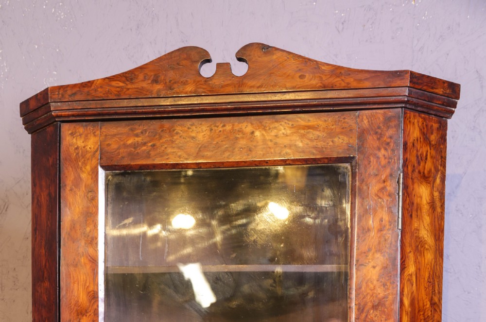 An antique corner cabinet crafted from figured yew wood featuring a single glazed door, decorative scroll pediment, and brass escutcheon. View II