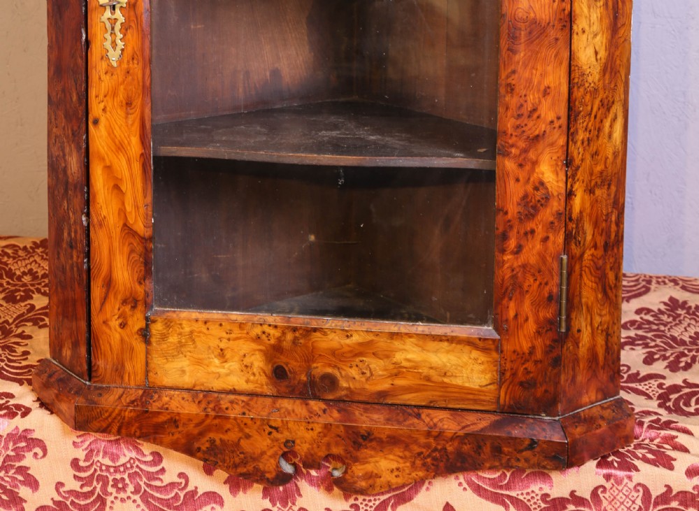 An antique corner cabinet crafted from figured yew wood featuring a single glazed door, decorative scroll pediment, and brass escutcheon. View III