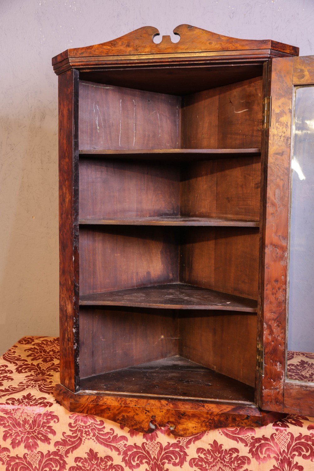 An antique corner cabinet crafted from figured yew wood featuring a single glazed door, decorative scroll pediment, and brass escutcheon. View IV