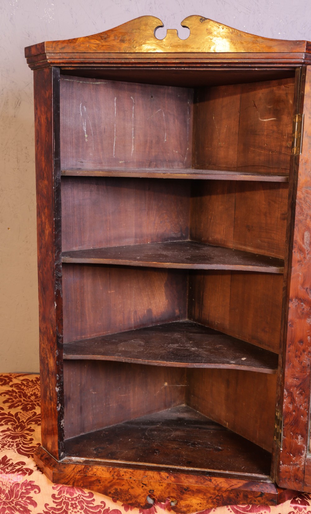An antique corner cabinet crafted from figured yew wood featuring a single glazed door, decorative scroll pediment, and brass escutcheon. View V