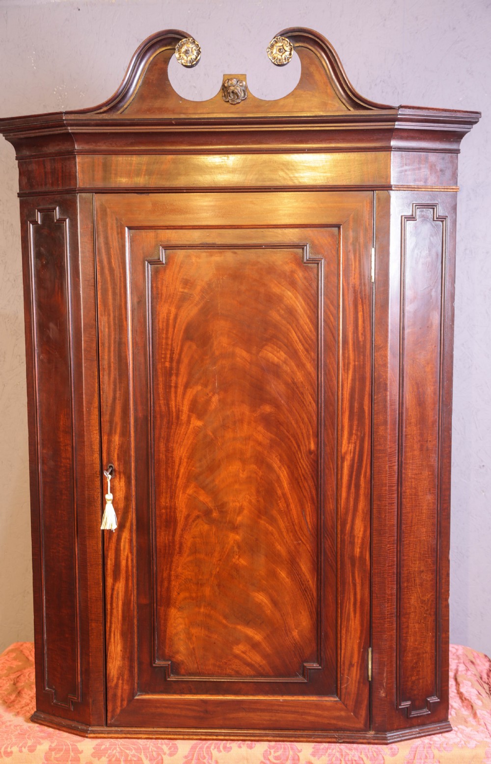 A Georgian mahogany corner cupboard featuring a swan-neck pediment with carved rosettes and a single flame mahogany panelled door.