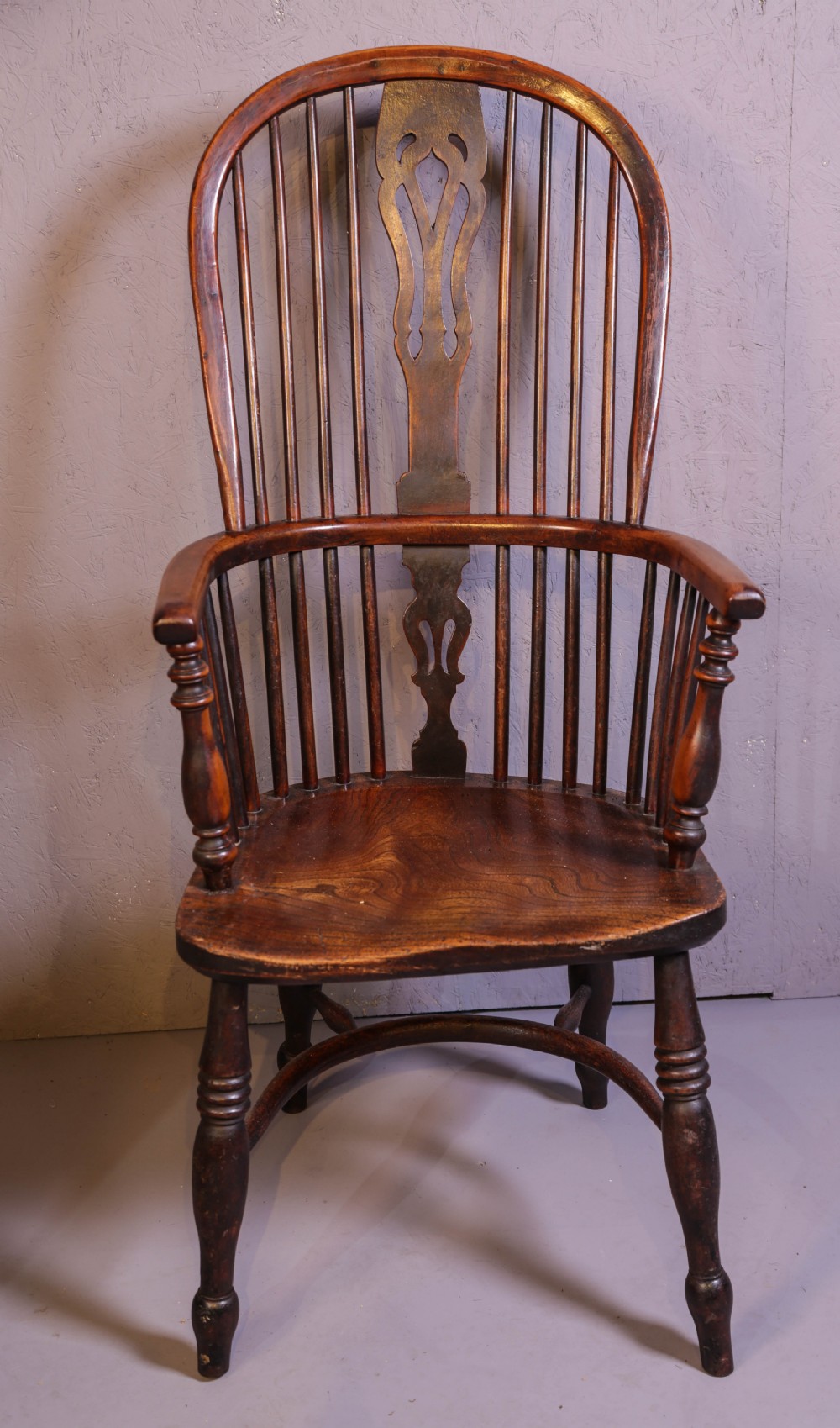 A high-back wooden Windsor armchair featuring a steam-bent hoop frame, a central pierced splat, turned legs, and a contoured elm saddle seat.