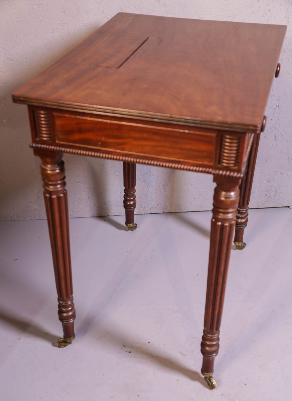An antique mahogany library table featuring turned reeded legs with brass castors, a single frieze drawer with turned wooden handles, and a rectangular top. View VI