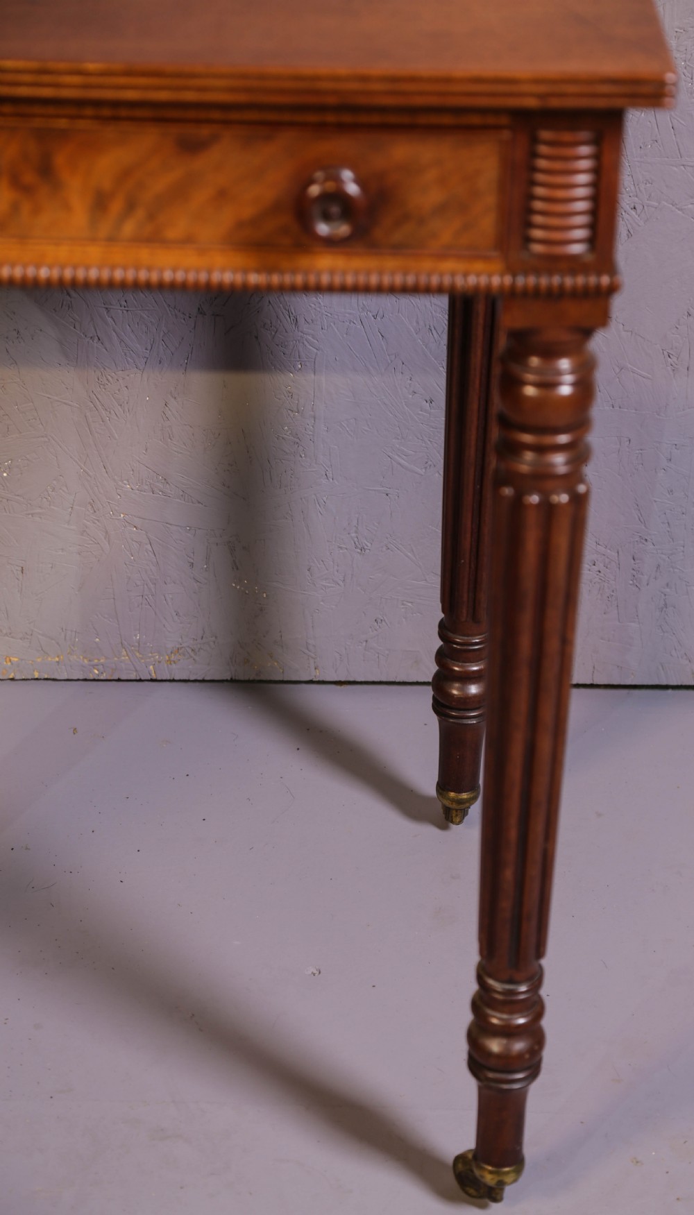 An antique mahogany library table featuring turned reeded legs with brass castors, a single frieze drawer with turned wooden handles, and a rectangular top. View XI