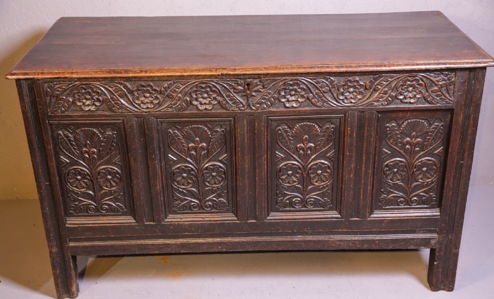 A dark brown oak coffer featuring four carved floral front panels beneath a carved lunette frieze.
