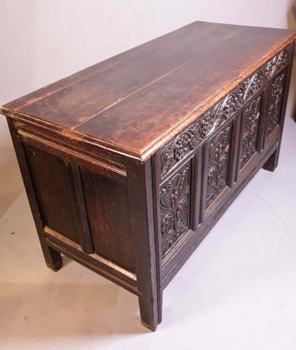 A dark brown oak coffer featuring four carved floral front panels beneath a carved lunette frieze. View II