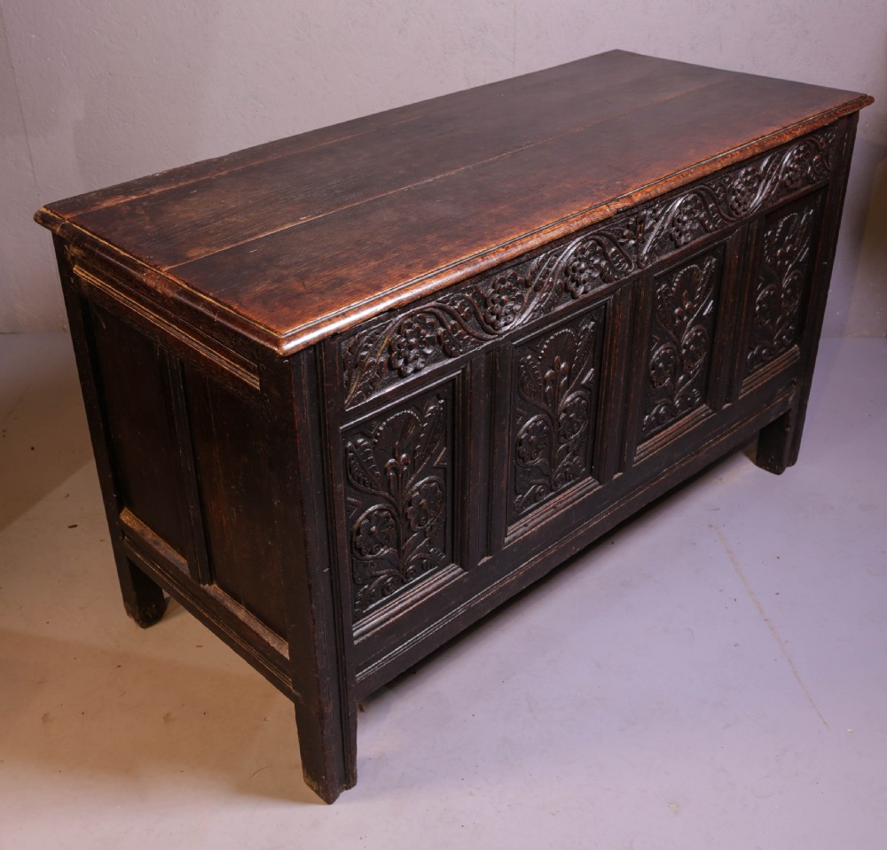 A dark brown oak coffer featuring four carved floral front panels beneath a carved lunette frieze. View III