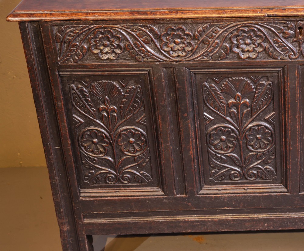 A dark brown oak coffer featuring four carved floral front panels beneath a carved lunette frieze. View IV