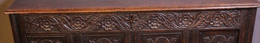 A dark brown oak coffer featuring four carved floral front panels beneath a carved lunette frieze. View V