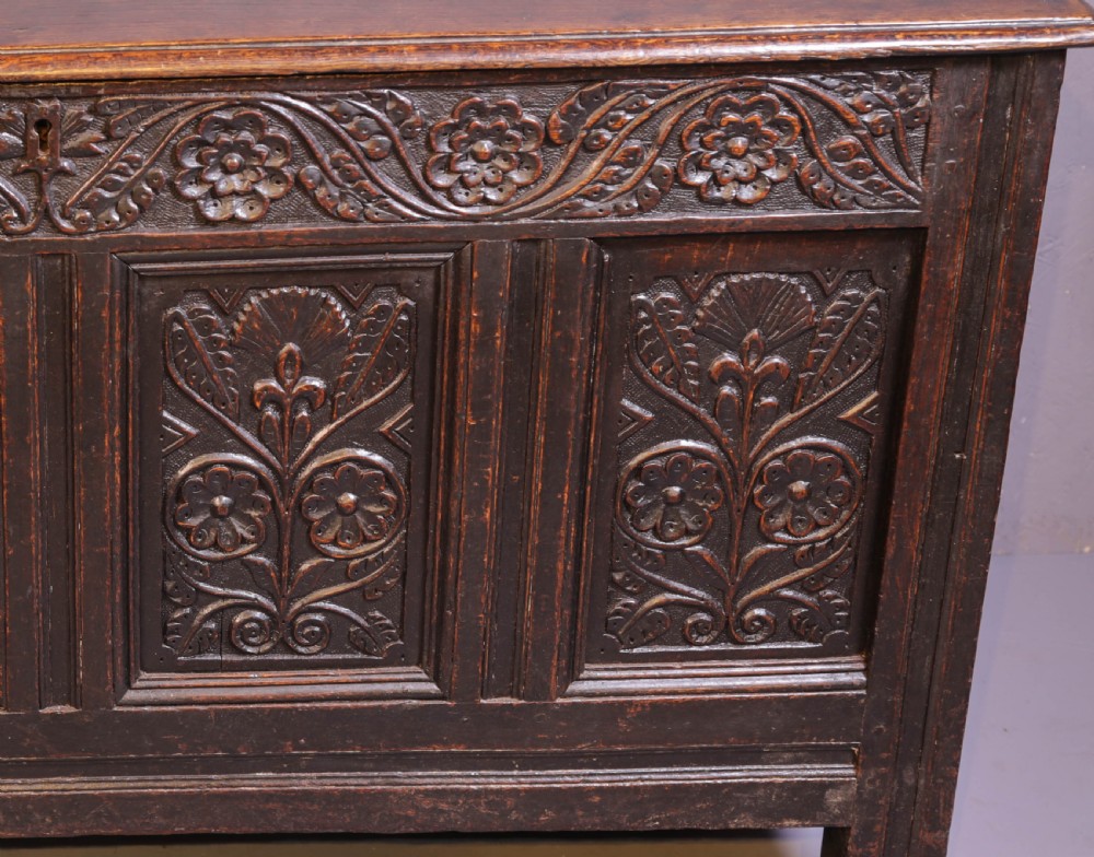 A dark brown oak coffer featuring four carved floral front panels beneath a carved lunette frieze. View VI