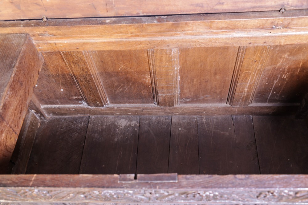 A dark brown oak coffer featuring four carved floral front panels beneath a carved lunette frieze. View XII