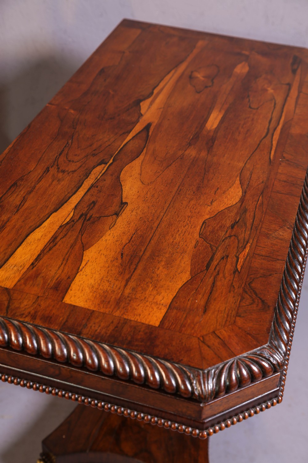 An antique Regency rosewood games table featuring a fold-over top with gadrooned trim, a turned pedestal support, and a quadform base with brass lion paw feet. View III