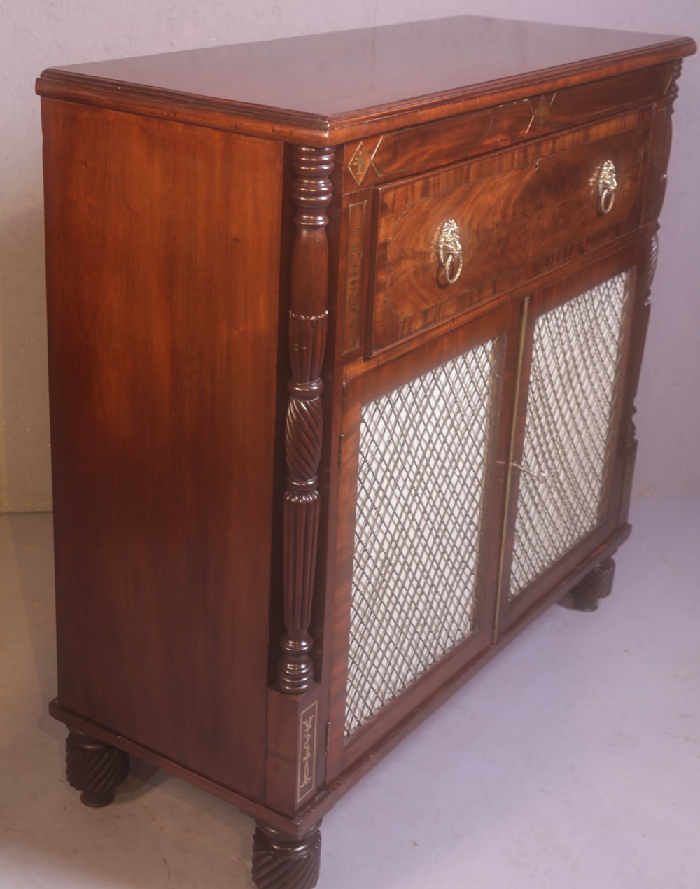 A Regency rosewood chiffonier with brass inlay, a long drawer featuring lion mask handles, and lower double doors with brass wire grilles over fabric. View II