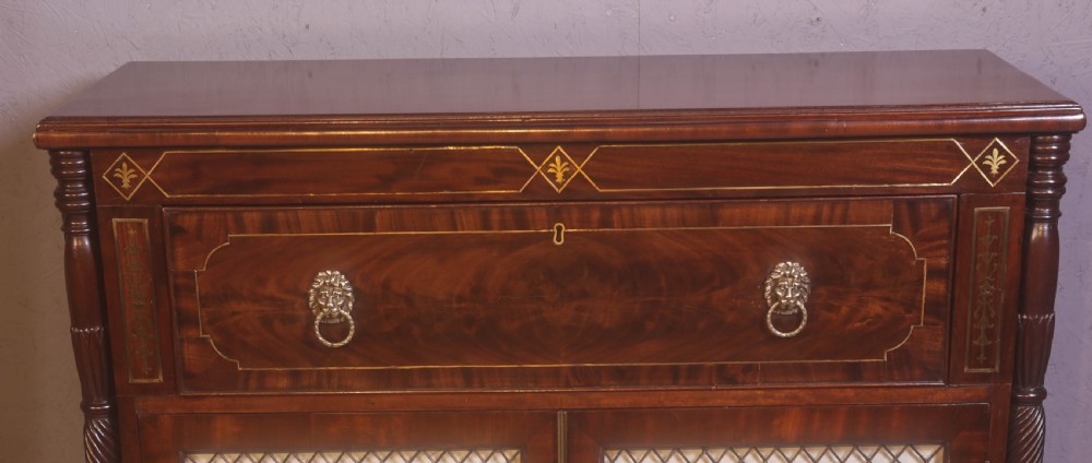 A Regency rosewood chiffonier with brass inlay, a long drawer featuring lion mask handles, and lower double doors with brass wire grilles over fabric. View VII