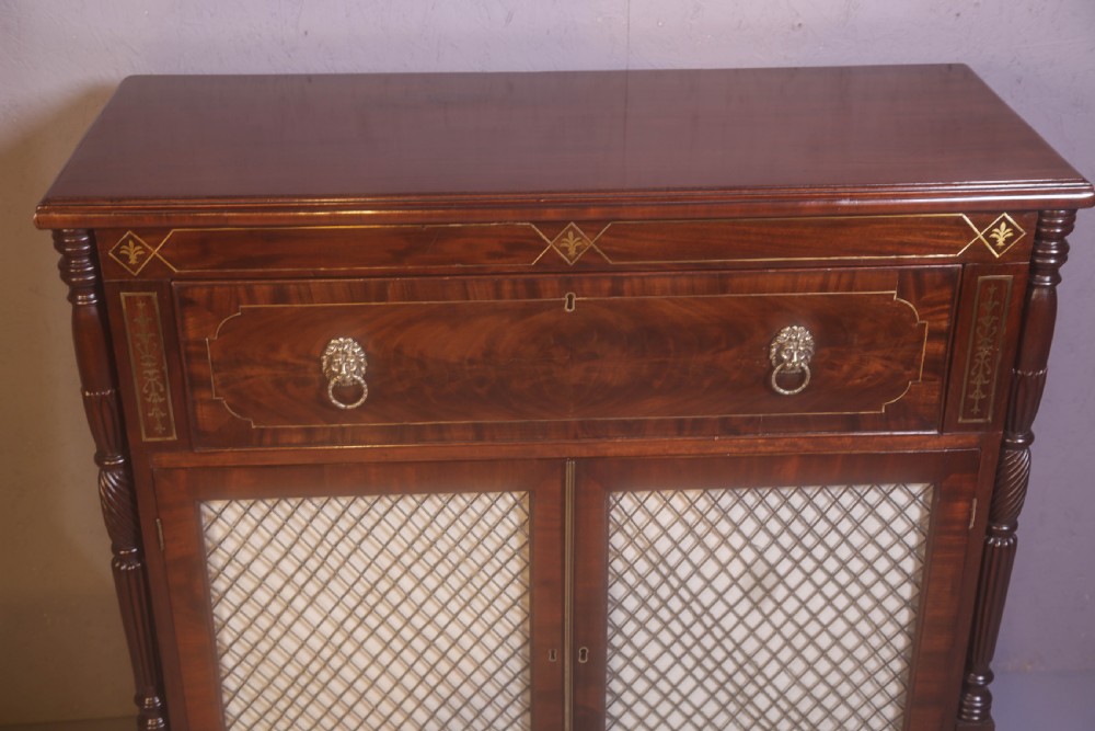 A Regency rosewood chiffonier with brass inlay, a long drawer featuring lion mask handles, and lower double doors with brass wire grilles over fabric. View IX