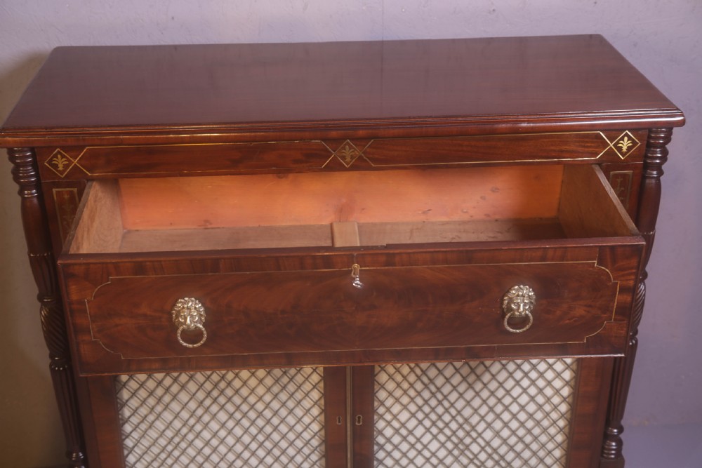 A Regency rosewood chiffonier with brass inlay, a long drawer featuring lion mask handles, and lower double doors with brass wire grilles over fabric. View X