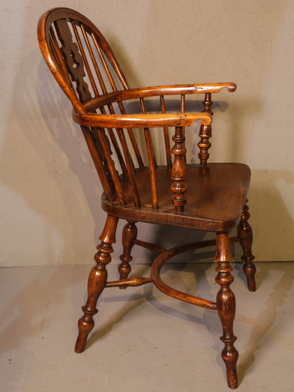 A low-back yew wood Windsor armchair featuring turned legs, a shaped saddle seat, a pierced burr splat, and a curved stretcher.