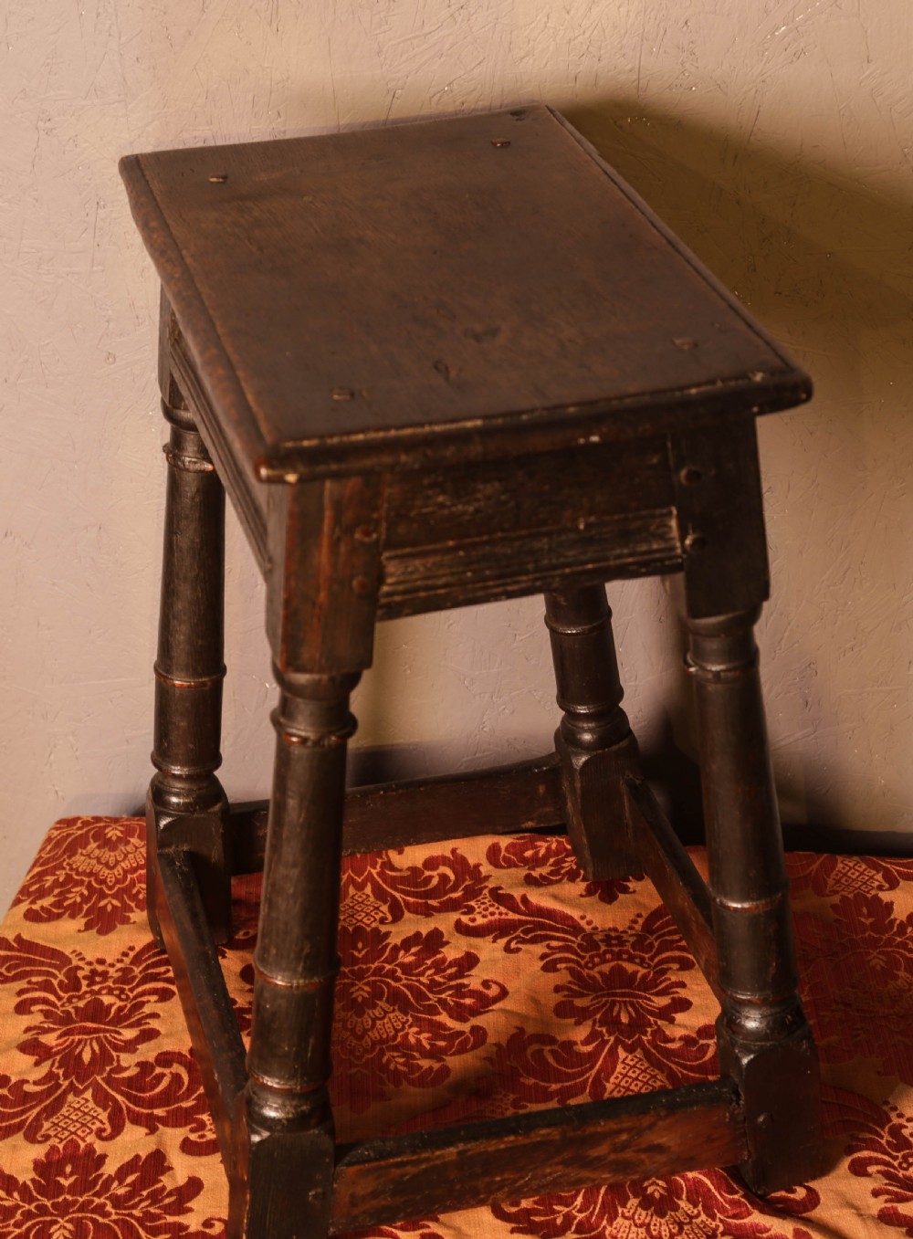 A seventeenth-century dark oak joint stool featuring turned legs, lower perimeter stretchers, and a flat top secured with wooden pegs. View III