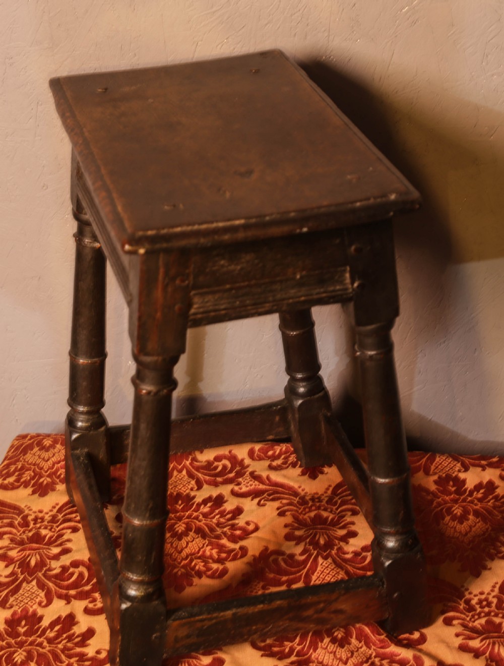 A seventeenth-century dark oak joint stool featuring turned legs, lower perimeter stretchers, and a flat top secured with wooden pegs. View VI