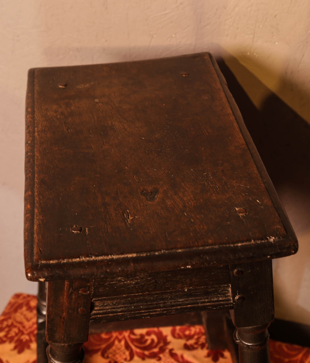 A seventeenth-century dark oak joint stool featuring turned legs, lower perimeter stretchers, and a flat top secured with wooden pegs. View VIII