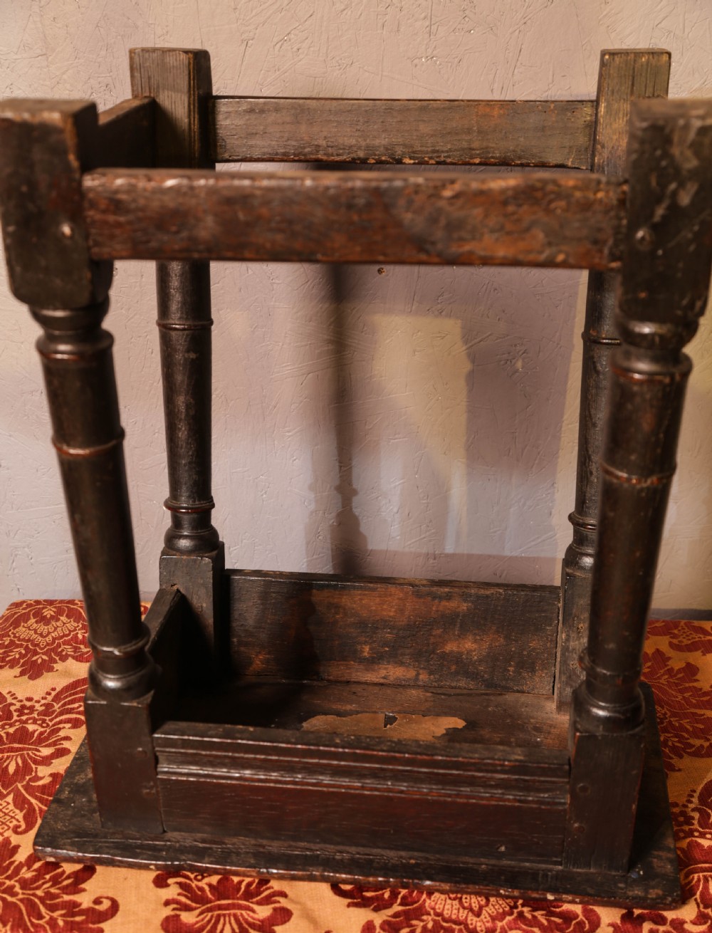 A seventeenth-century dark oak joint stool featuring turned legs, lower perimeter stretchers, and a flat top secured with wooden pegs. View IX