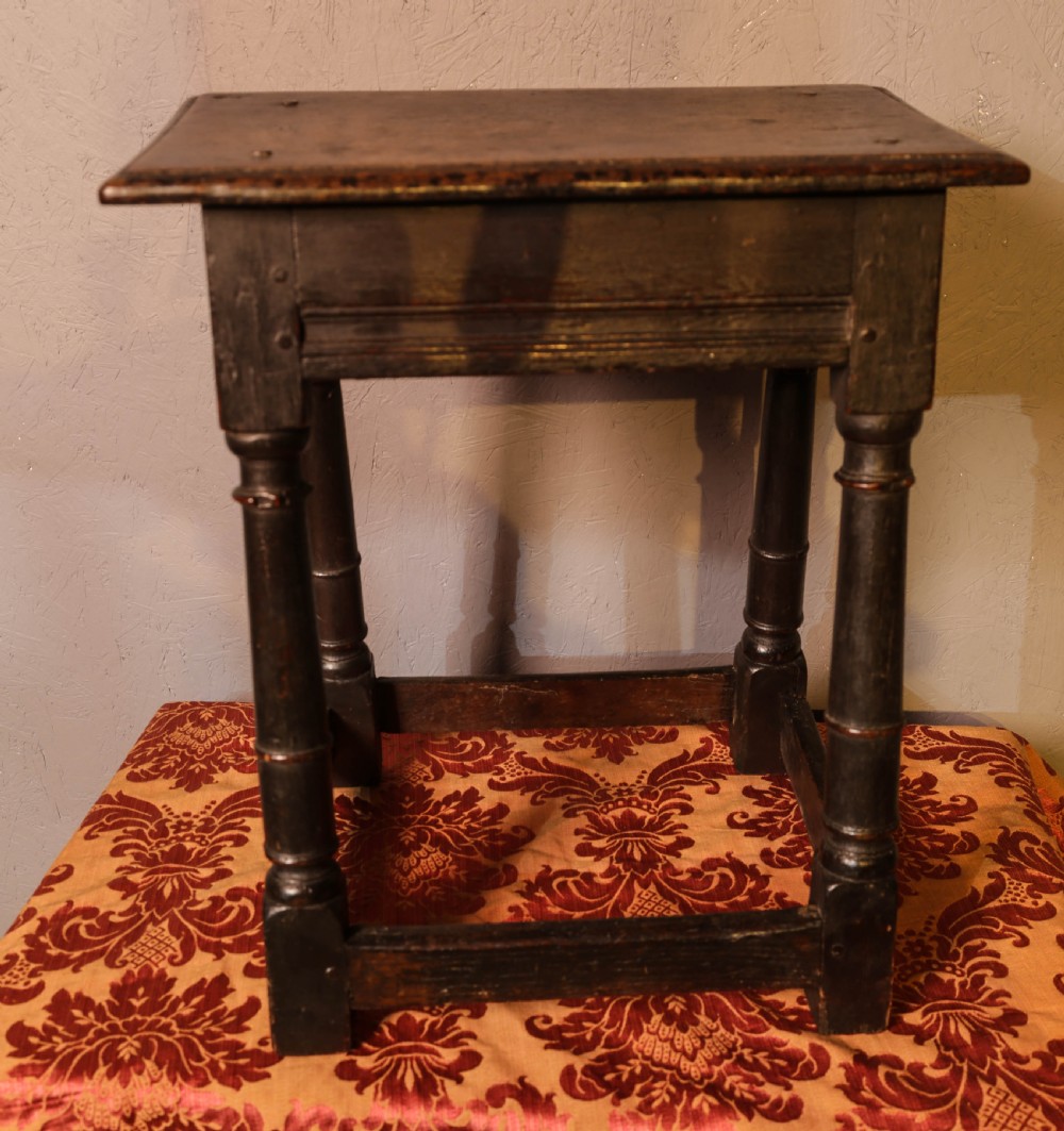 A seventeenth-century dark oak joint stool featuring turned legs, lower perimeter stretchers, and a flat top secured with wooden pegs. View XI