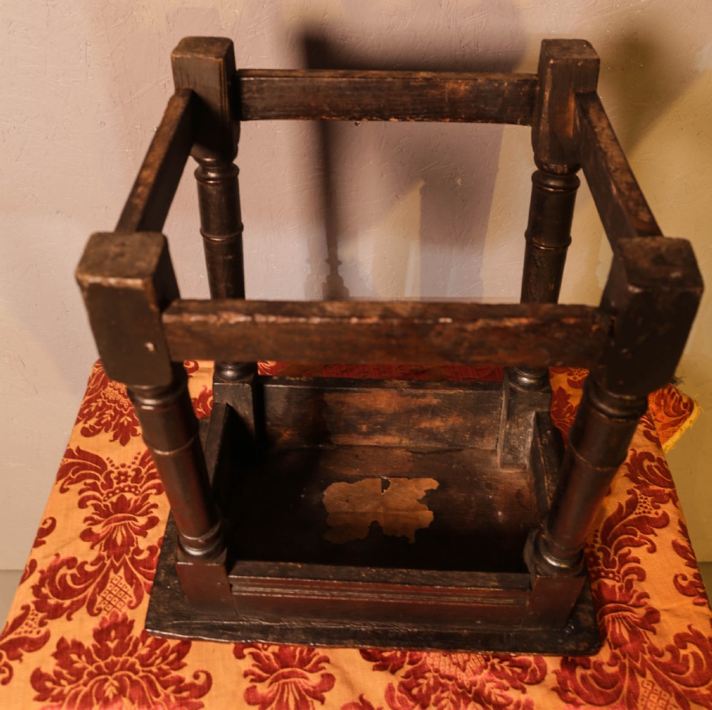 A seventeenth-century dark oak joint stool featuring turned legs, lower perimeter stretchers, and a flat top secured with wooden pegs. View XII