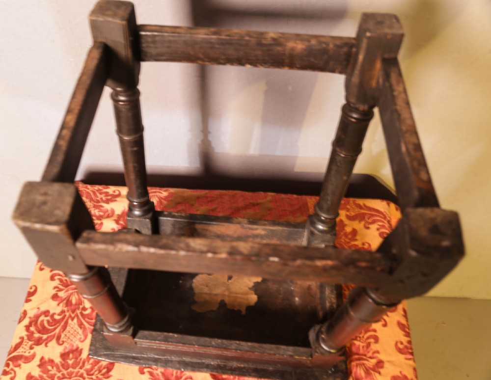 A seventeenth-century dark oak joint stool featuring turned legs, lower perimeter stretchers, and a flat top secured with wooden pegs. View XIII