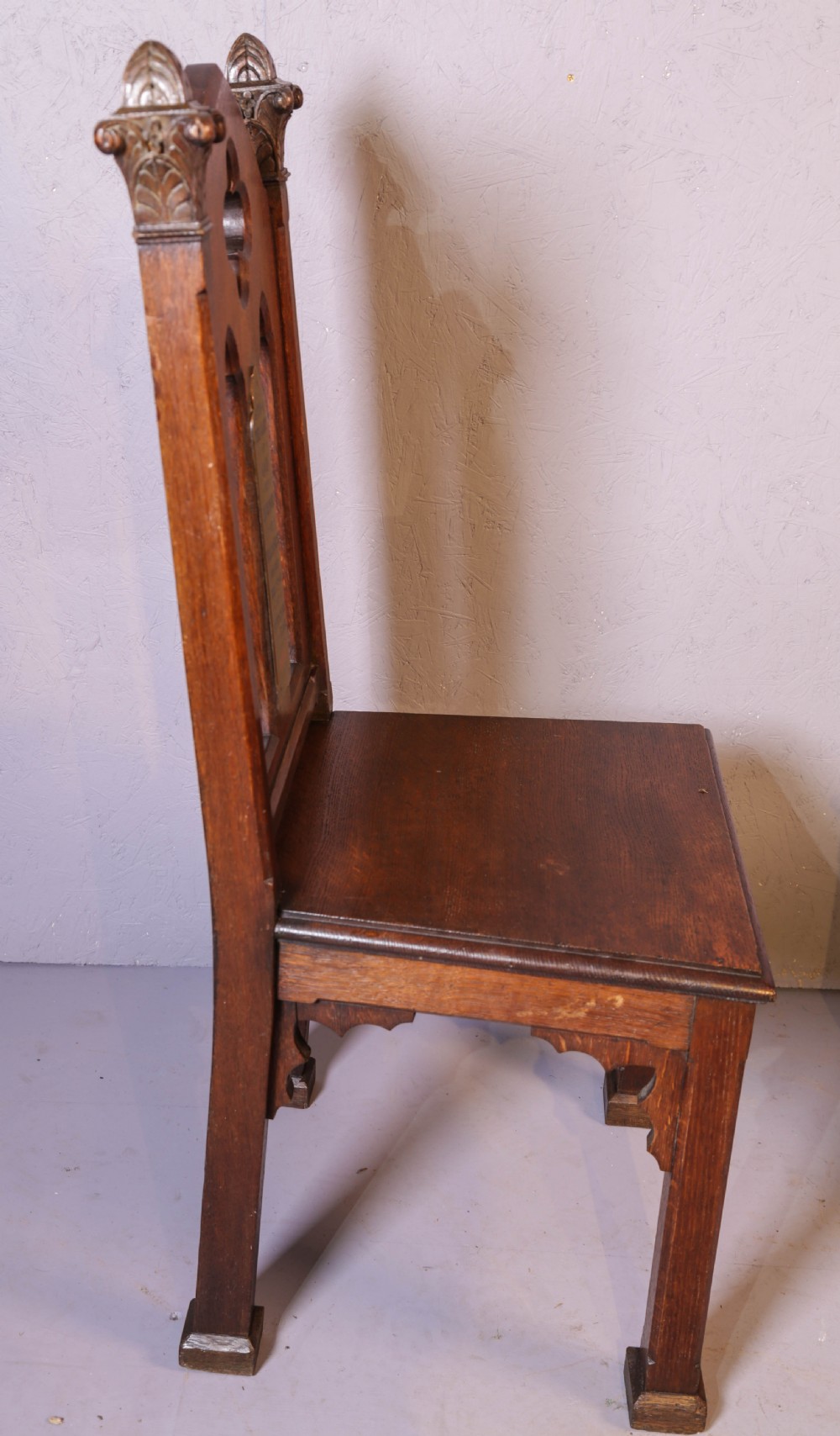 A pair of dark oak Gothic Revival church chairs featuring pointed arch backs, carved trefoil tracery, decorative corner finials, and central brass memorial plaques. View VIII