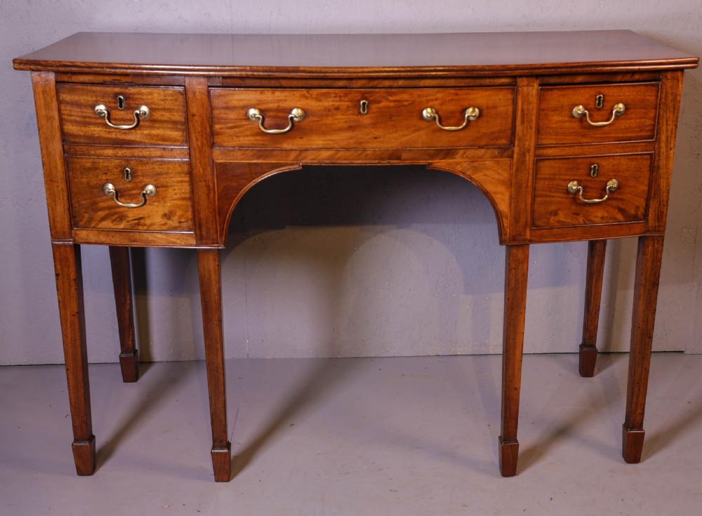 A Georgian mahogany bowfront sideboard featuring a central arched aperture, drawer storage with brass swan-neck handles, and square tapered legs.