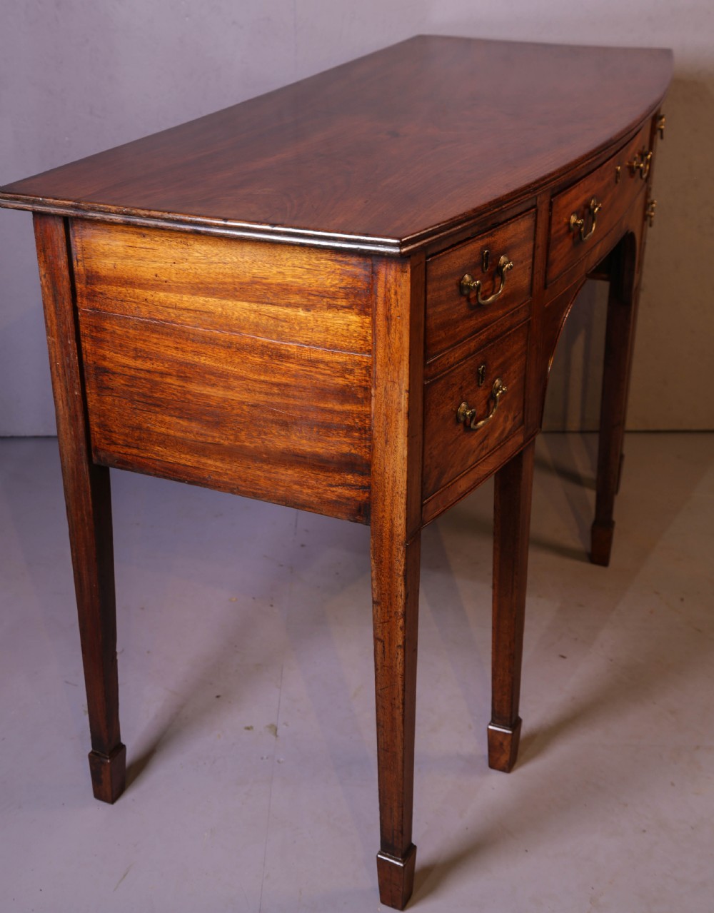 A Georgian mahogany bowfront sideboard featuring a central arched aperture, drawer storage with brass swan-neck handles, and square tapered legs. View II