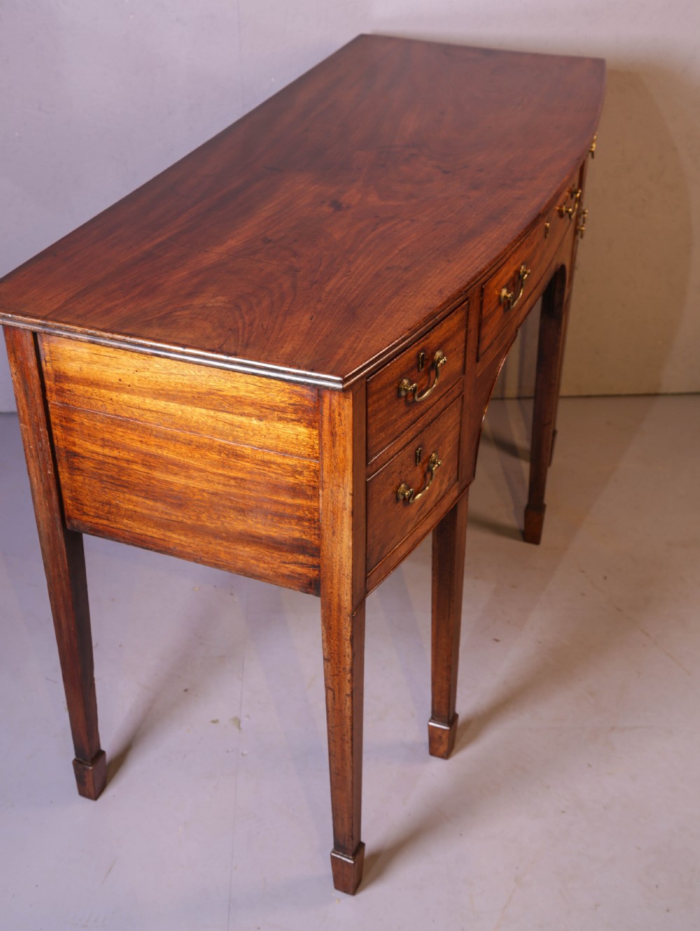 A Georgian mahogany bowfront sideboard featuring a central arched aperture, drawer storage with brass swan-neck handles, and square tapered legs. View III