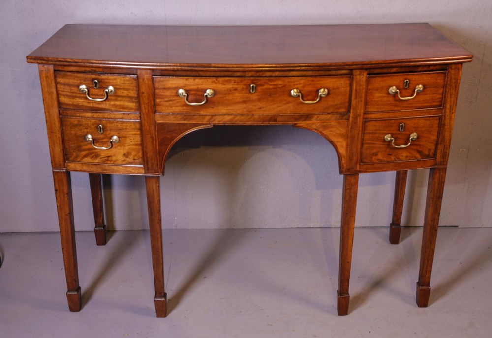 A Georgian mahogany bowfront sideboard featuring a central arched aperture, drawer storage with brass swan-neck handles, and square tapered legs. View V