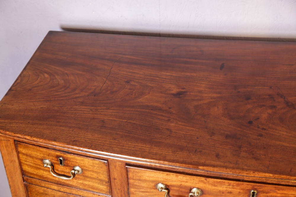 A Georgian mahogany bowfront sideboard featuring a central arched aperture, drawer storage with brass swan-neck handles, and square tapered legs. View IX
