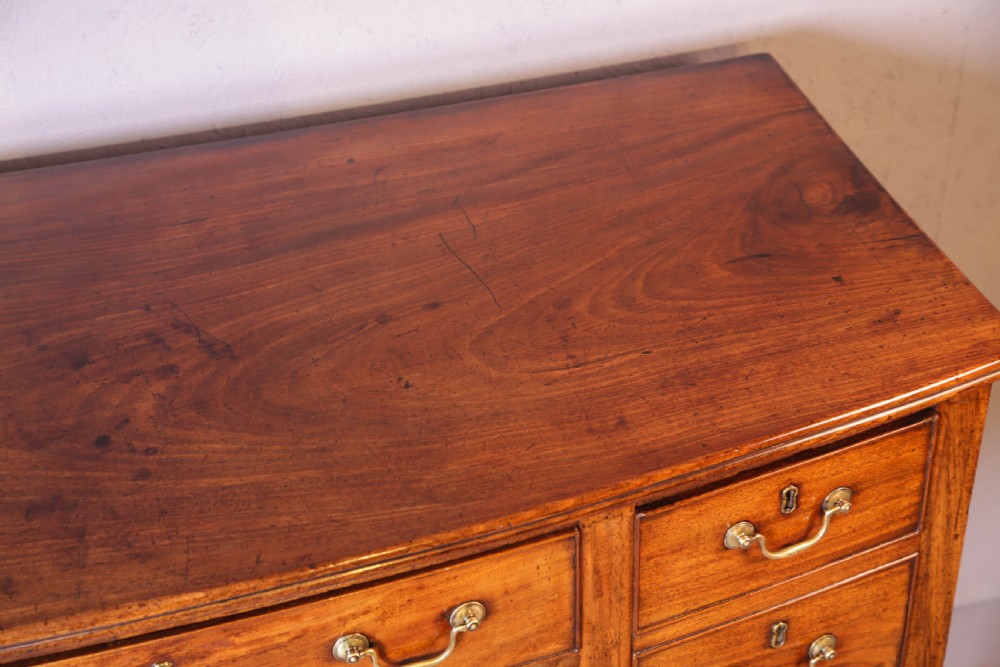 A Georgian mahogany bowfront sideboard featuring a central arched aperture, drawer storage with brass swan-neck handles, and square tapered legs. View X