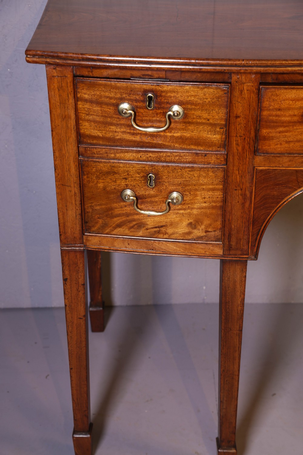 A Georgian mahogany bowfront sideboard featuring a central arched aperture, drawer storage with brass swan-neck handles, and square tapered legs. View XII
