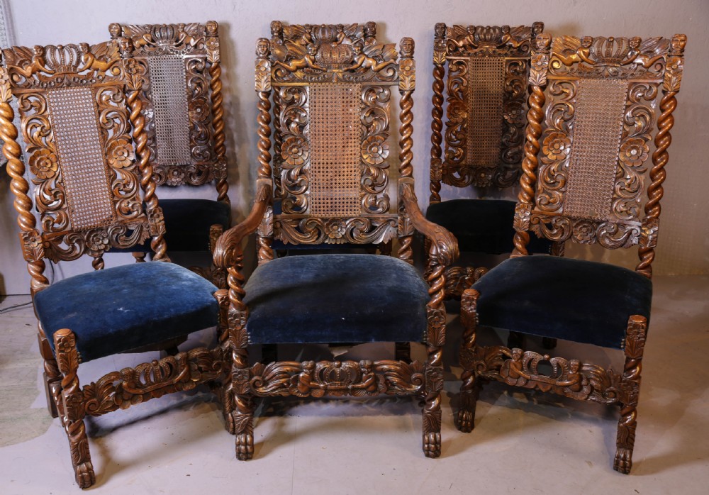 Set of six high-backed Carolean style walnut dining chairs featuring intricate scroll and crown carvings, barley twist pillars, cane back panels, and blue velvet upholstered seats.