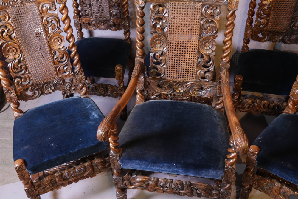 Set of six high-backed Carolean style walnut dining chairs featuring intricate scroll and crown carvings, barley twist pillars, cane back panels, and blue velvet upholstered seats. View V