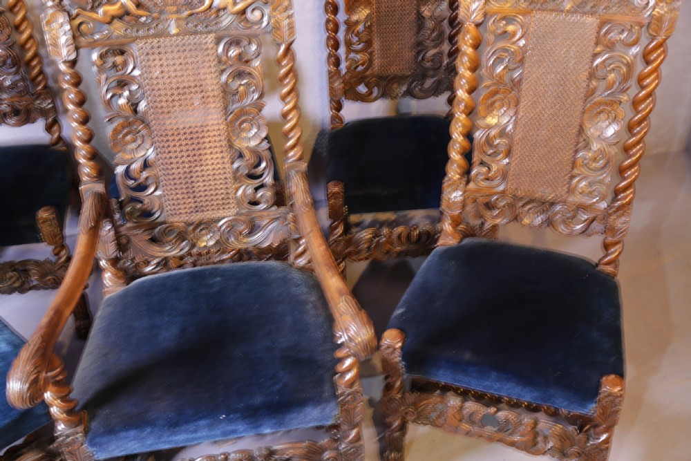 Set of six high-backed Carolean style walnut dining chairs featuring intricate scroll and crown carvings, barley twist pillars, cane back panels, and blue velvet upholstered seats. View VI