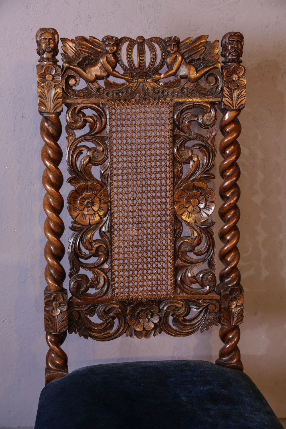 Set of six high-backed Carolean style walnut dining chairs featuring intricate scroll and crown carvings, barley twist pillars, cane back panels, and blue velvet upholstered seats. View VII