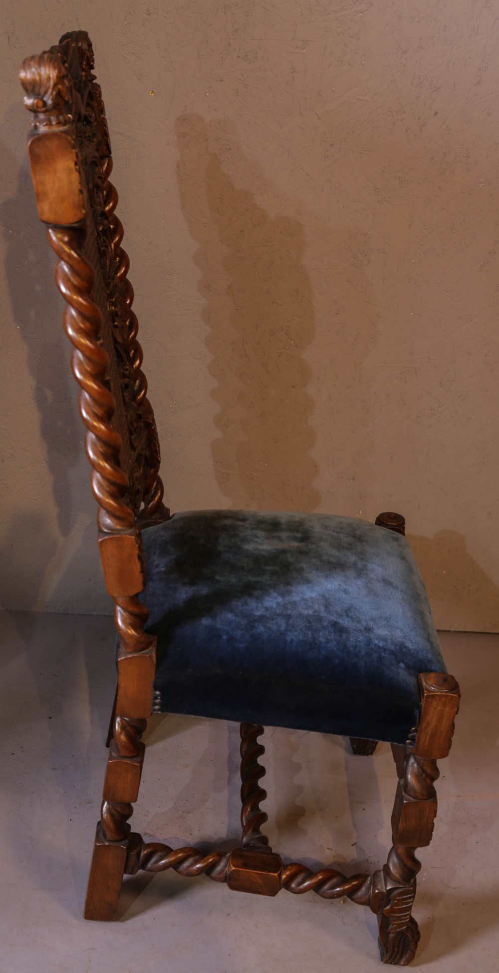 Set of six high-backed Carolean style walnut dining chairs featuring intricate scroll and crown carvings, barley twist pillars, cane back panels, and blue velvet upholstered seats. View X