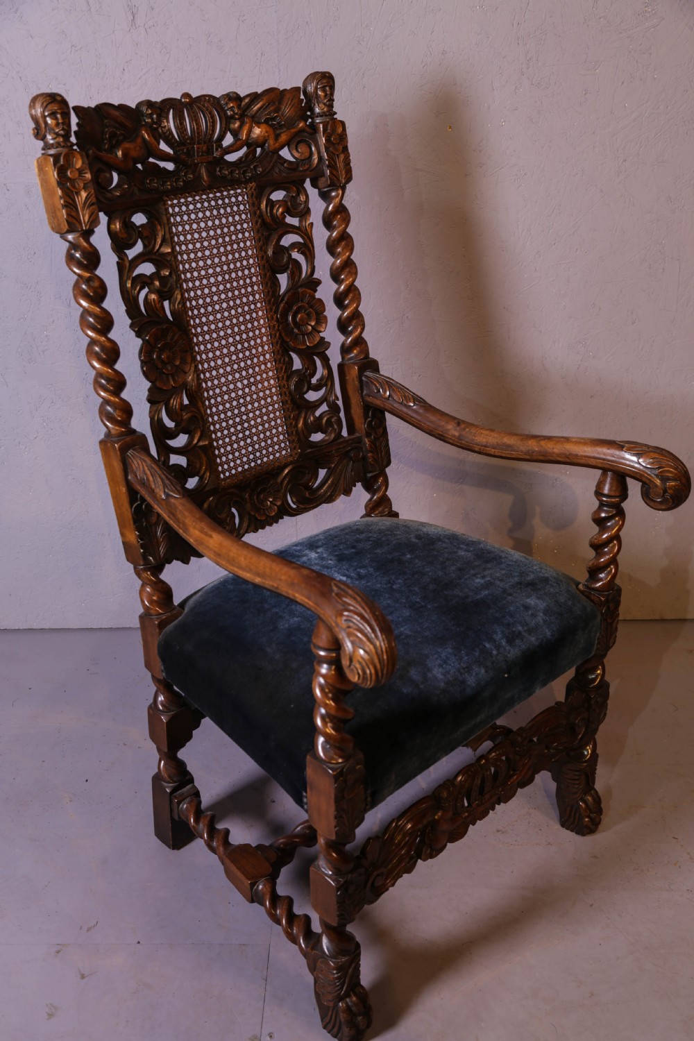 Set of six high-backed Carolean style walnut dining chairs featuring intricate scroll and crown carvings, barley twist pillars, cane back panels, and blue velvet upholstered seats. View XIII