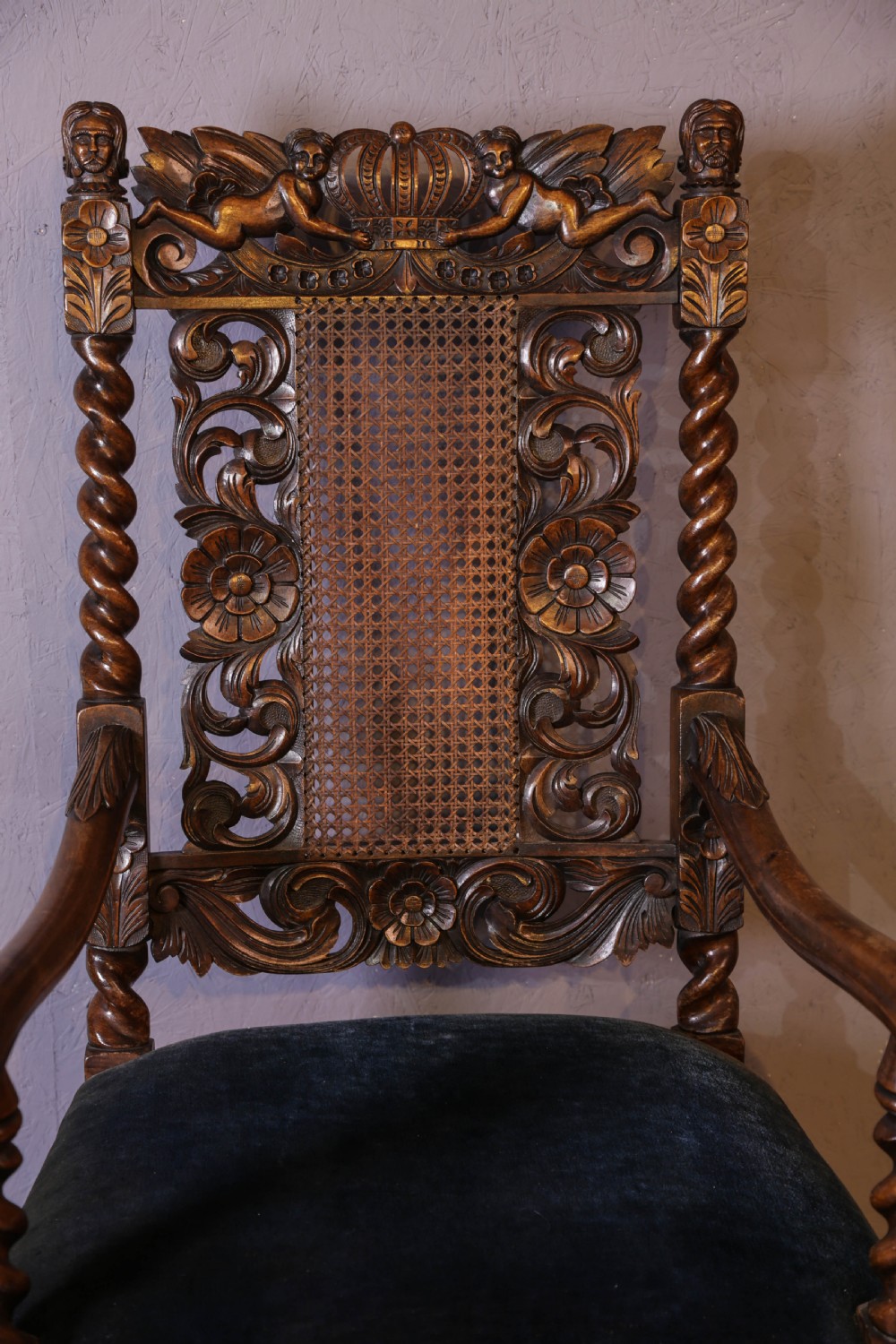 Set of six high-backed Carolean style walnut dining chairs featuring intricate scroll and crown carvings, barley twist pillars, cane back panels, and blue velvet upholstered seats. View XVI